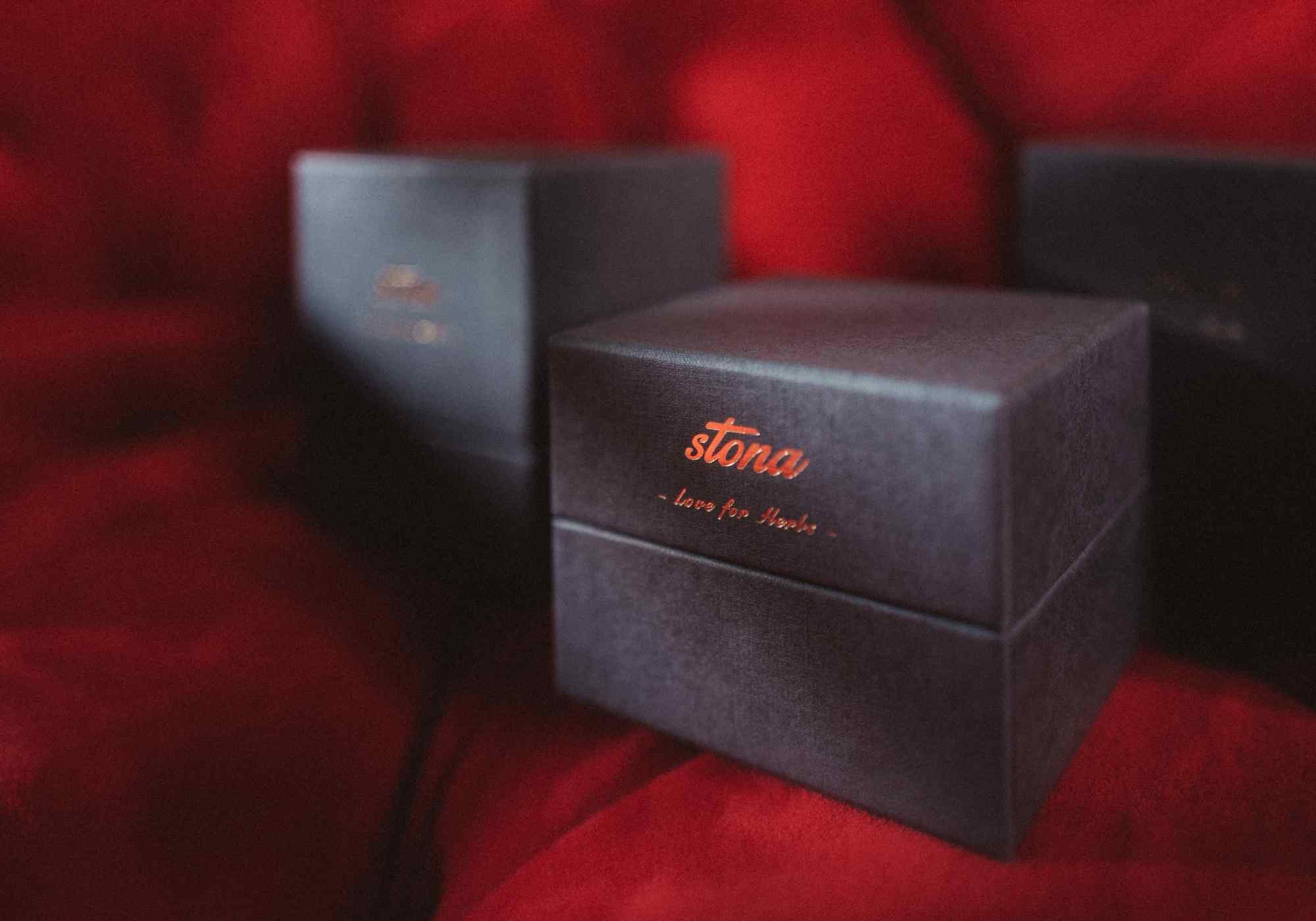 Antracite gift packaging box with 'stona' branding on a red textured background